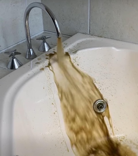 Discoloured water running from a household tap, showing why water system maintenance matters