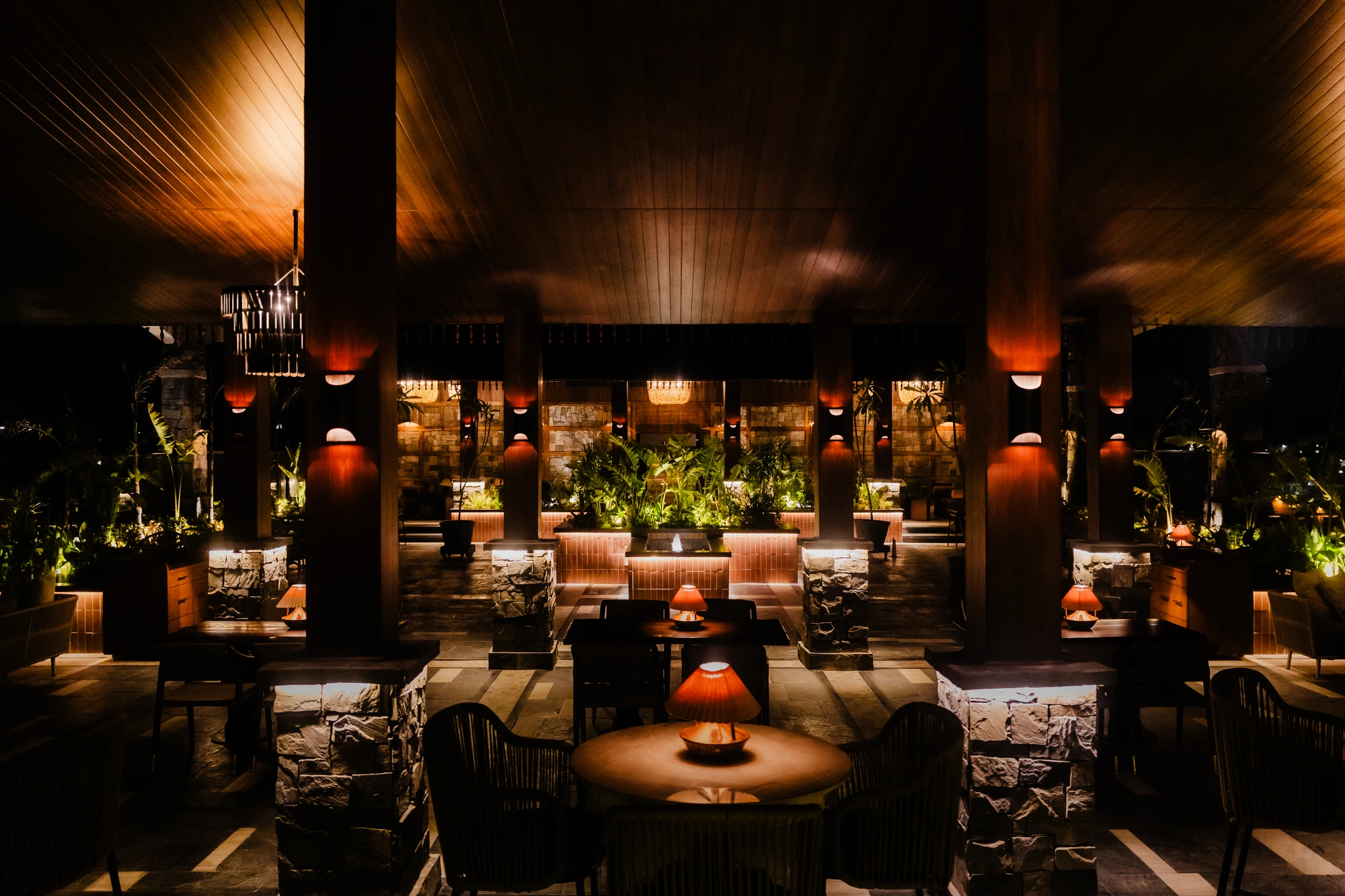 Upstairs dining room with timber ceilings, stone-clad columns, greenery and warmly lit tables.