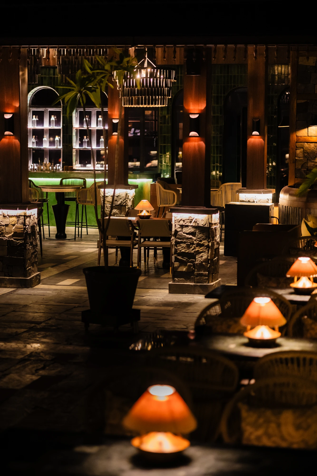 Warm table lamps lead through Upstairs, past stone-and-timber pillars towards the green bar.